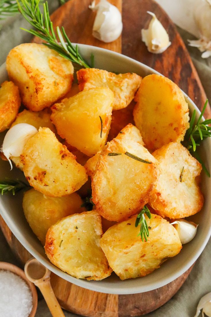 a white bowl filled with potatoes on top of a wooden cutting board next to garlic