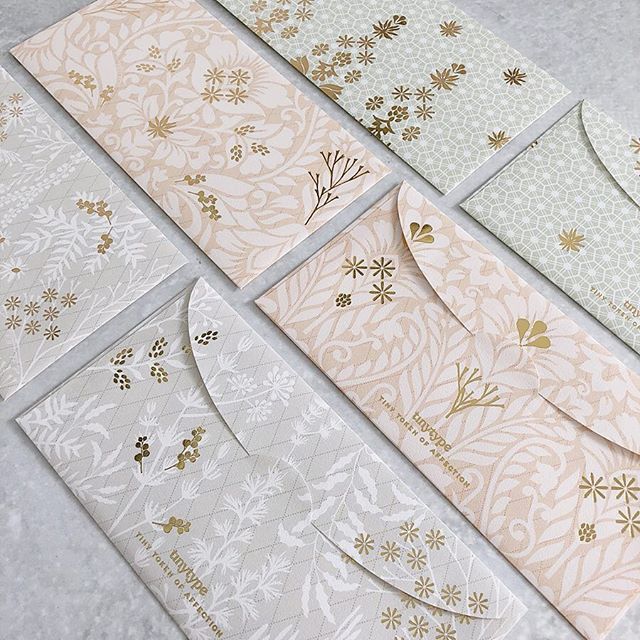 four different colored envelopes with gold and white designs on them, all lined up together