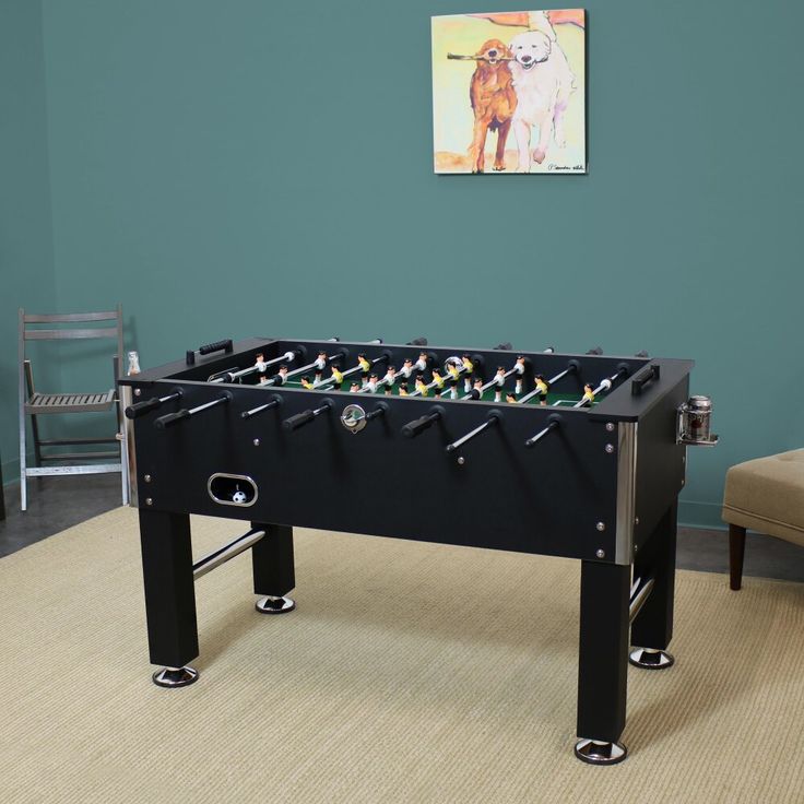 a foosball table in the corner of a room with chairs and a painting on the wall