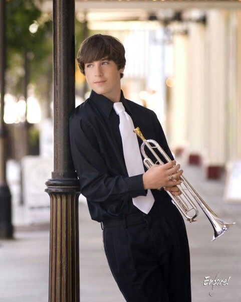 a young man in a suit and tie holding a trumpet leaning against a lamp post