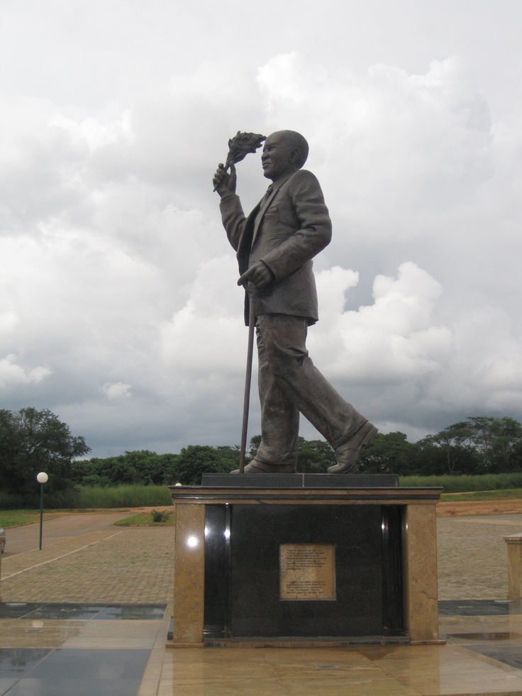 a statue of a man holding a camera in front of a cloudy sky with clouds