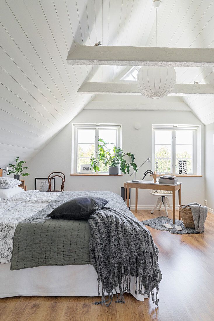 an attic bedroom with white walls and wood flooring is furnished with natural light from the windows