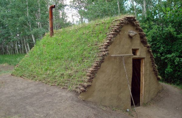 a small house made out of grass with a door in the center and a green roof