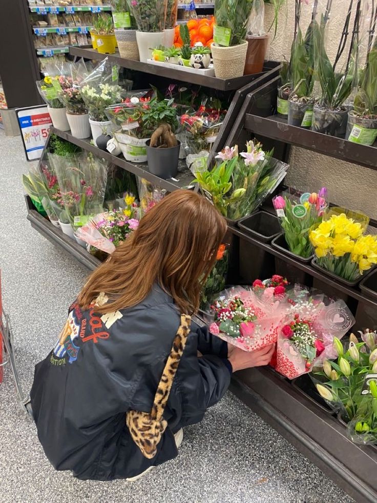 a woman kneeling down to pick up flowers in a flower shop with lots of potted plants