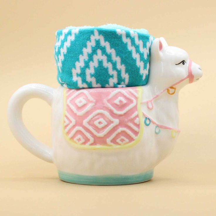 a ceramic teapot with a pink and blue cow on it's side, sitting on a beige surface