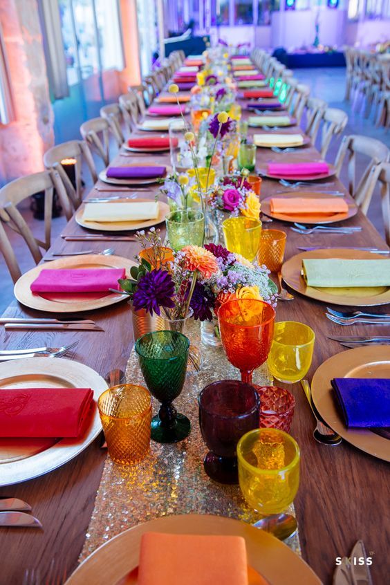 a long table is set with colorful dishes and place settings for the guests to enjoy