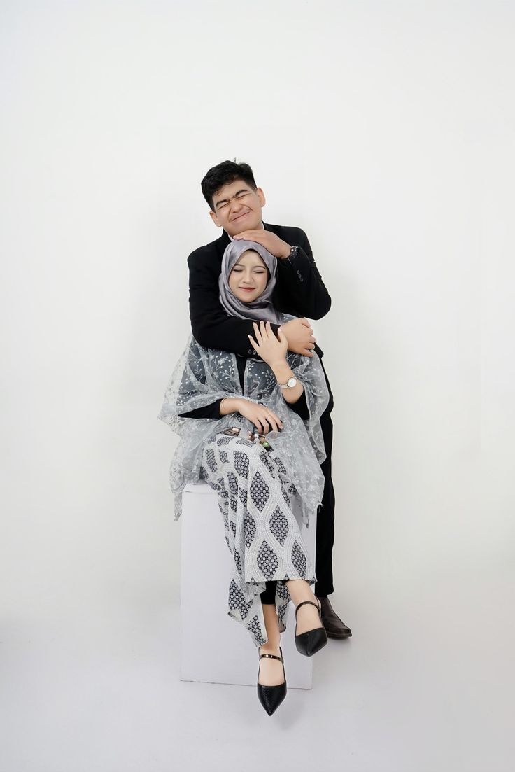 a man and woman sitting on top of each other in front of a white background