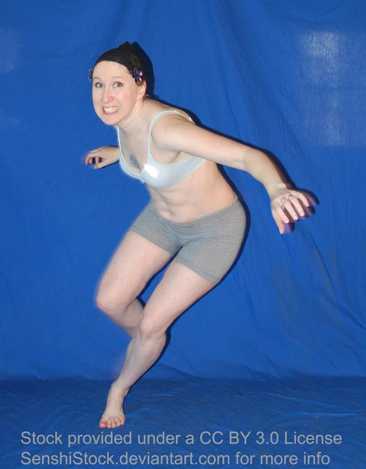 a woman in grey shorts and white shirt jumping up into the air with her arms outstretched