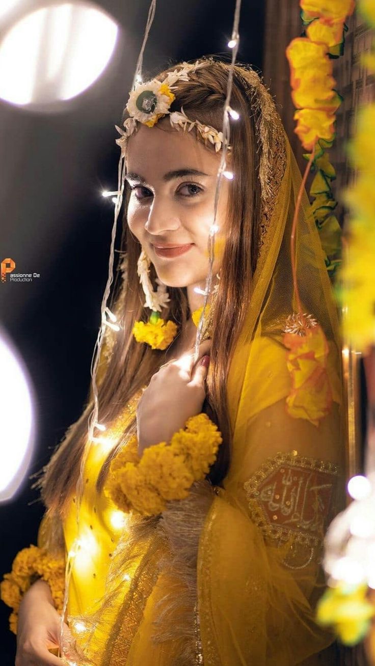 a woman dressed in yellow is posing for the camera with flowers on her head and veil