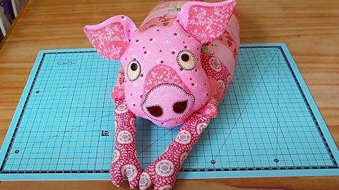 a pink stuffed pig laying on top of a cutting board next to a pair of scissors