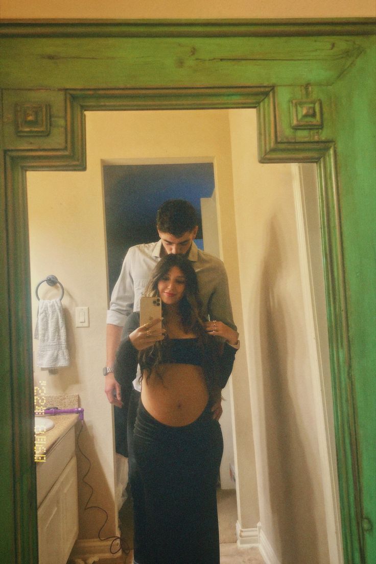 a man and woman standing in front of a mirror looking at their pregnant bellys