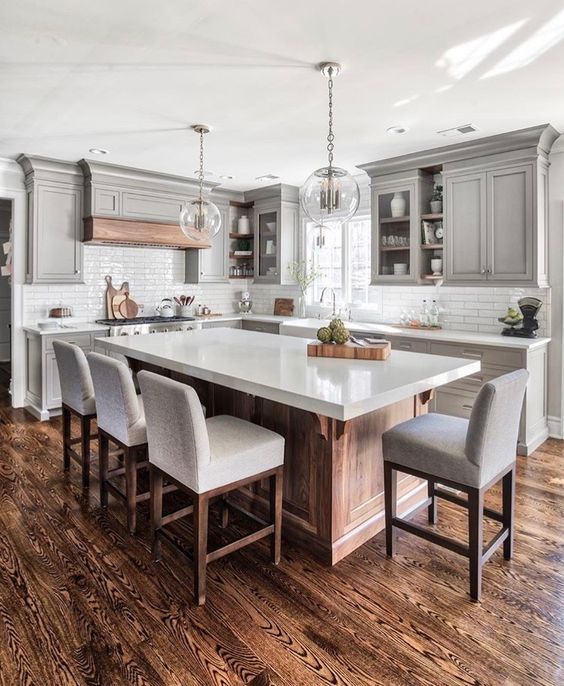 a large kitchen with an island in the middle and chairs at the end, surrounded by gray cabinets