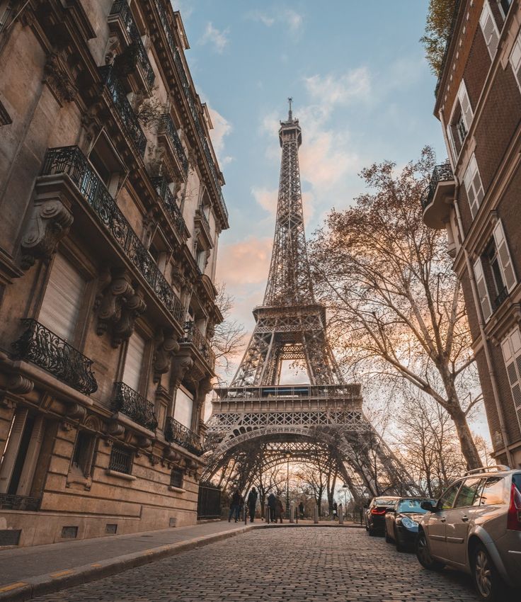 the eiffel tower towering over cars parked in front of it's buildings