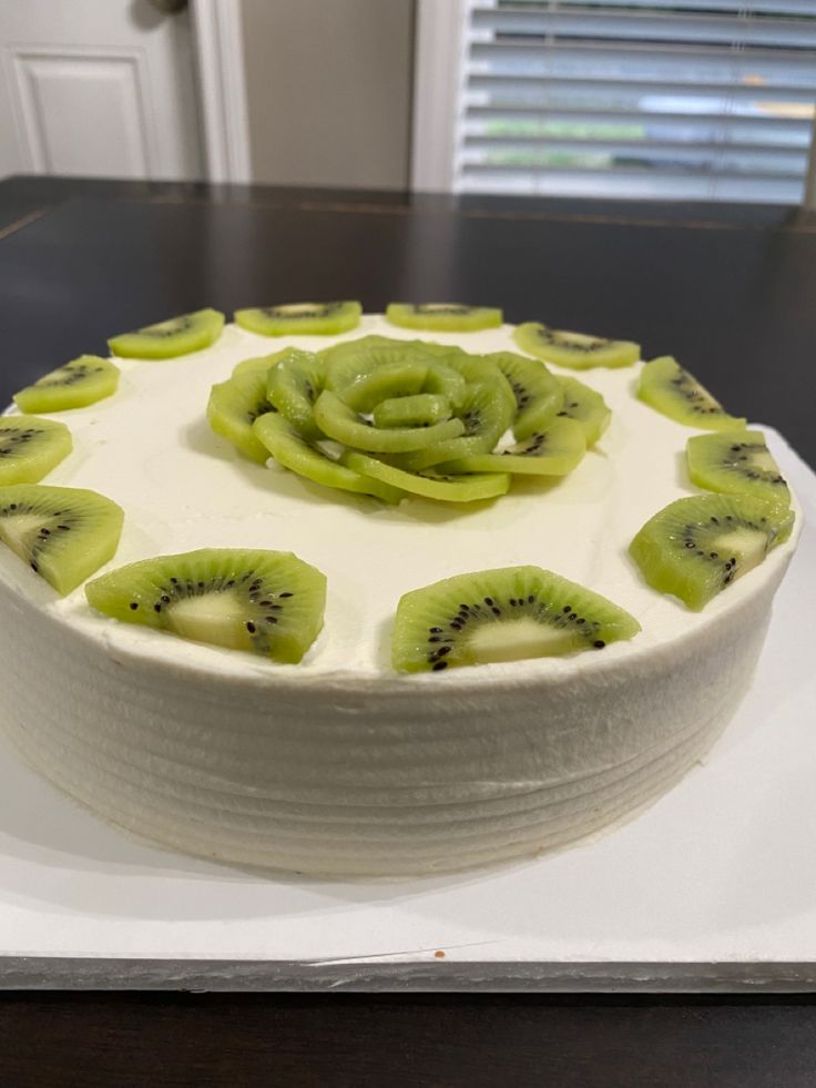 a cake with kiwi slices on it sitting on top of a white platter