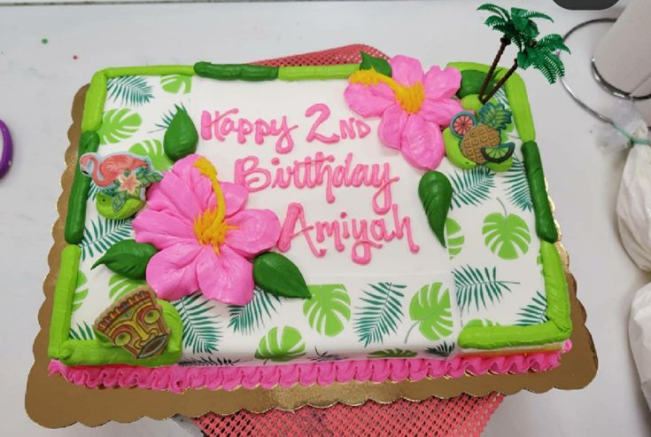 a birthday cake with pink flowers and green leaves on the top is sitting on a table