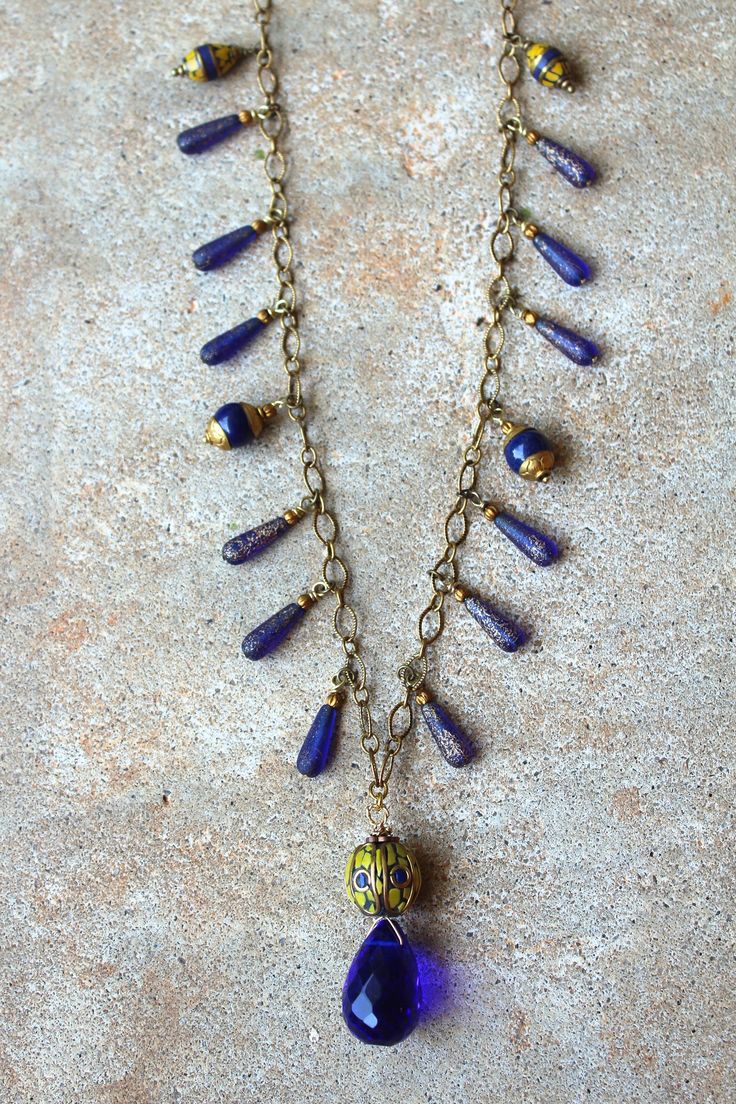 "Cobalt blue Czech glass drops paired with Tibetan beads and a vintage teardrop crystal on a gold chain. 32\" chain with a 2\" pendant. Lobster claw clasp. Handmade. One of a kind." Blue Beaded Brass Necklaces, Blue Teardrop Pendant Necklace With Adjustable Chain, Blue Teardrop Necklace With Adjustable Chain, Gold Teardrop Beaded Necklaces With Dangling Beads, Gold Teardrop Beaded Necklace With Dangling Beads, Blue Pendant Jewelry With Dangling Beads, Blue Dangling Beads Pendant Jewelry, Vintage Blue Teardrop Necklace, Handmade Blue Necklaces With Long Drop Shape