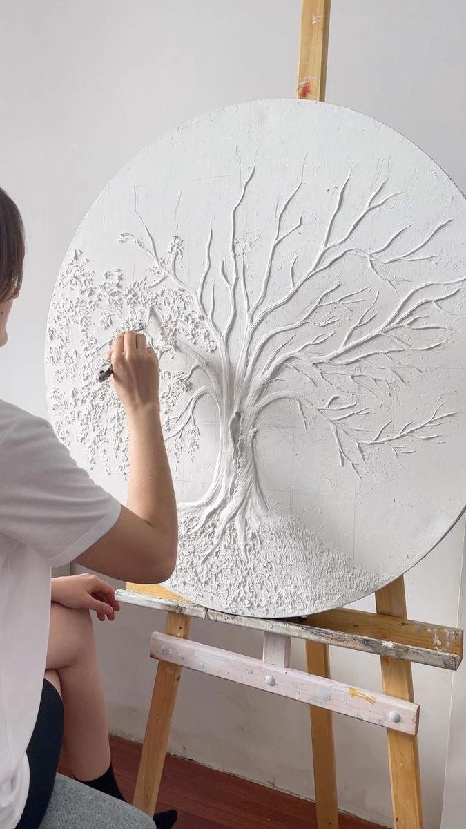 a woman is painting a tree on a large white piece of art that she is holding