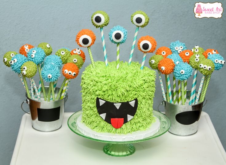 a green cake with monster decorations on it and cupcakes in the shape of eyes