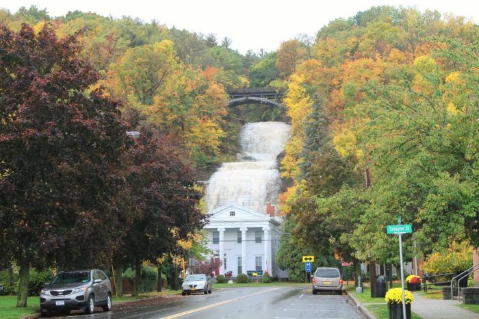 cars are driving down the road in front of a waterfall