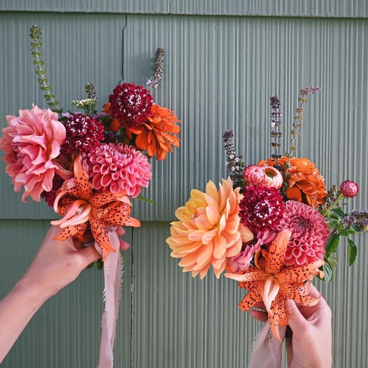 two hands holding bouquets of flowers in front of a green wall with peeling paint