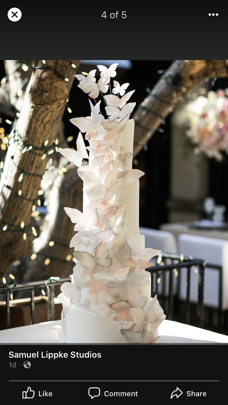 a white wedding cake sitting on top of a table next to a tree with lights