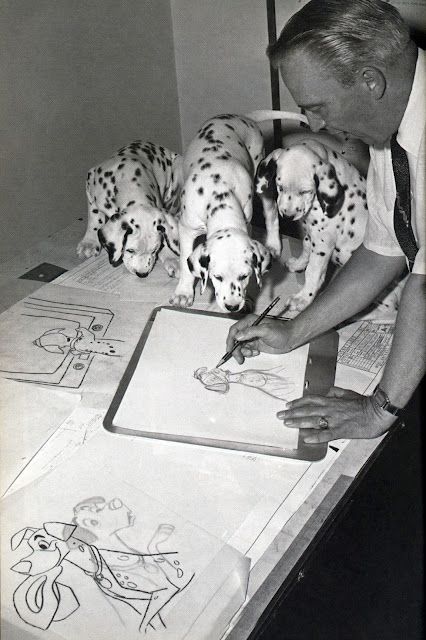 a man is drawing with dalmatian puppies in front of him on a table