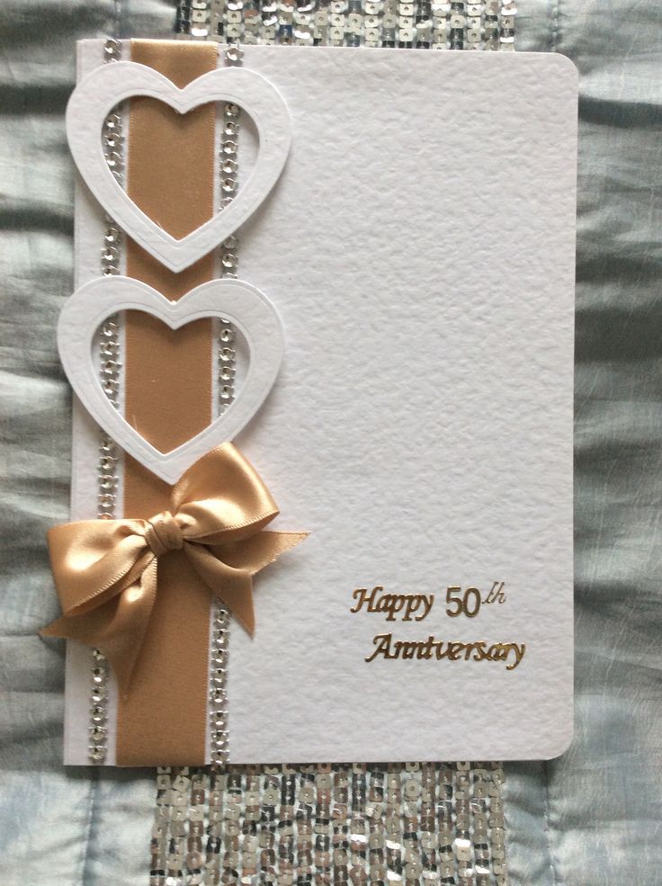 an anniversary card with two hearts and a bow on the front, sitting on top of a quilt