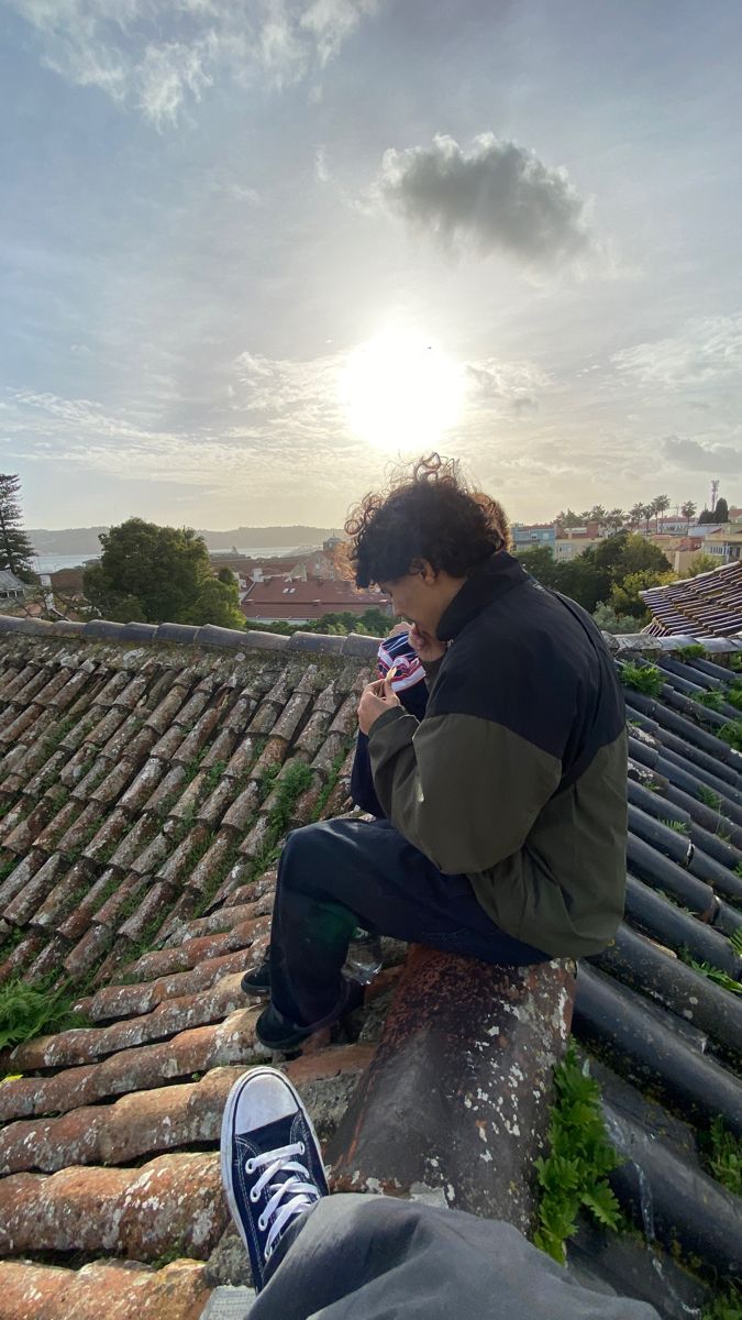 a man sitting on top of a roof looking at his cell phone