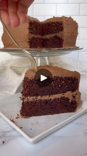 a slice of chocolate cake on a plate with a fork in it and someone cutting into the cake