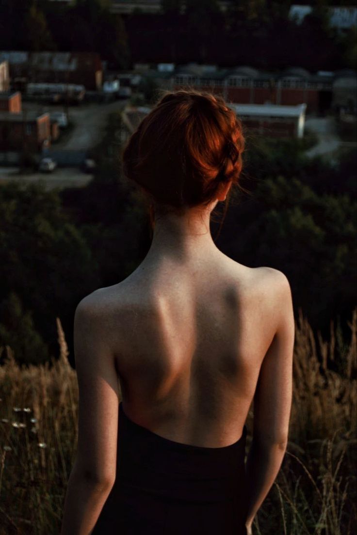 the back of a woman in a black dress looking out over tall grass and trees