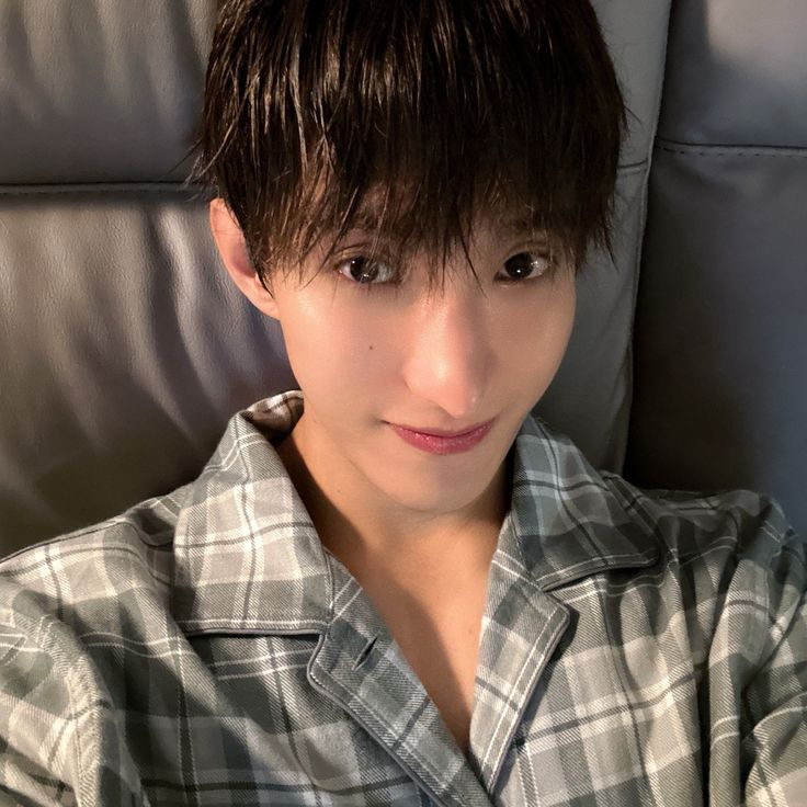 a woman with short hair sitting on a couch wearing a plaid shirt and looking at the camera