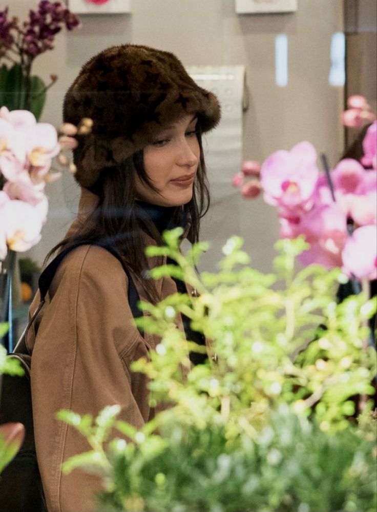 a woman wearing a fur hat looking at flowers