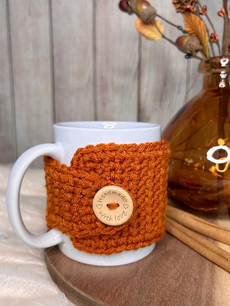 a crocheted coffee cup cozys up next to a vase with dried flowers