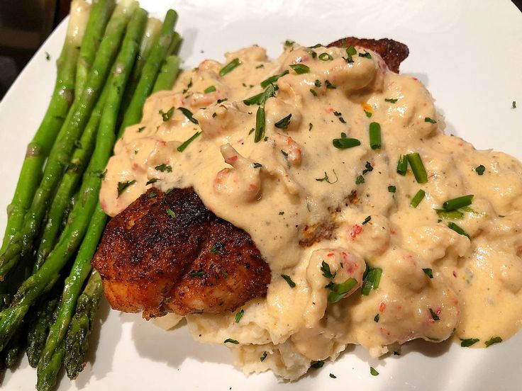 a white plate topped with meat covered in gravy and asparagus spears