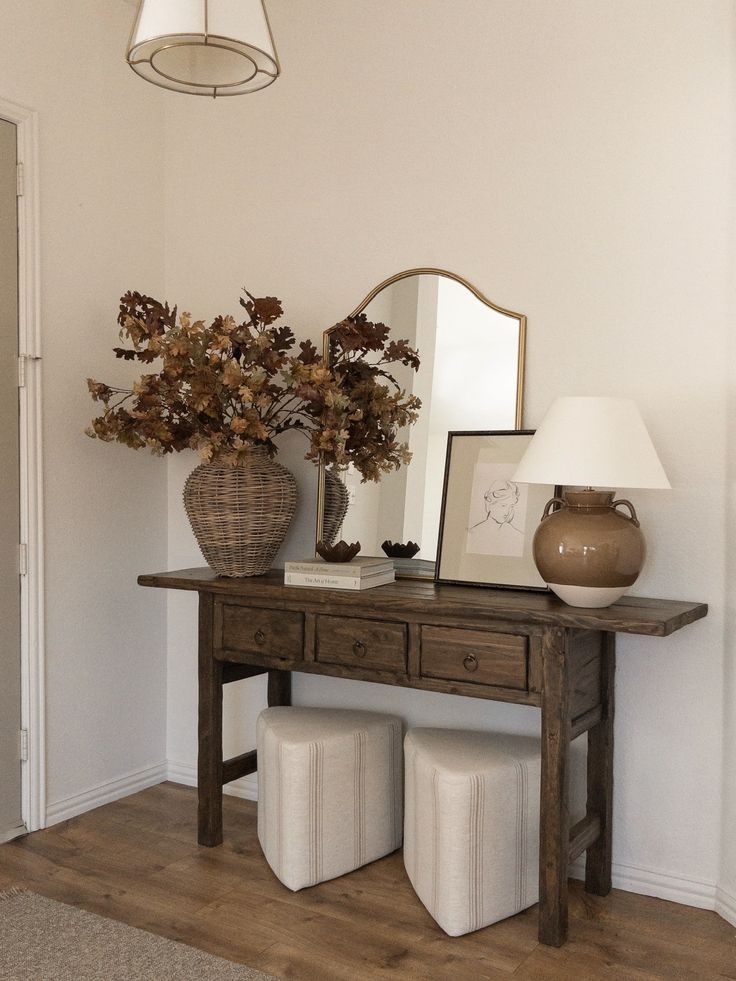 a wooden table topped with two vases filled with flowers next to a mirror and lamp