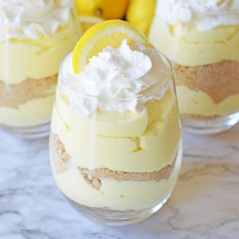 two glasses filled with dessert sitting on top of a marble counter next to lemons