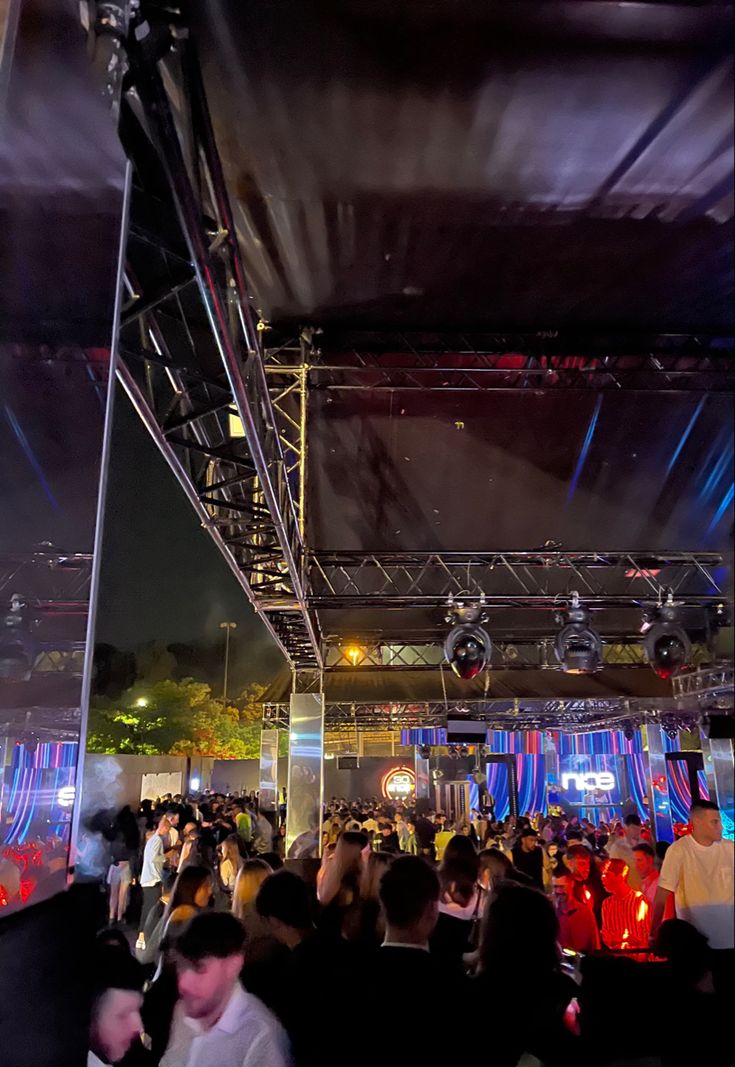 a large group of people standing around in front of a stage with lights on it