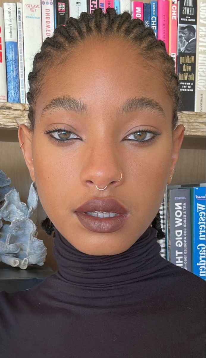 a woman with braids on her head standing in front of bookshelves and looking at the camera