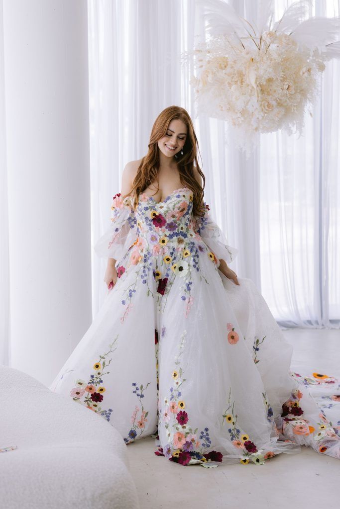 a woman in a white dress with flowers on the skirt is posing for a photo