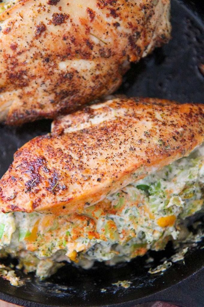 two pieces of chicken sitting on top of a pan covered in broccoli and cheese