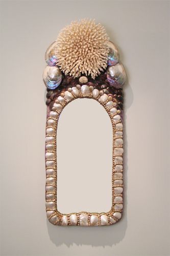 a mirror that is on the wall with shells around it and a flower in the middle