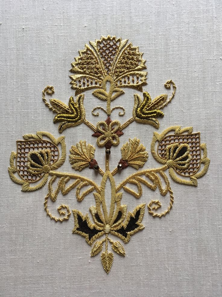 an embroidered design on a white cloth with gold trimmings and decorative flowers in the center