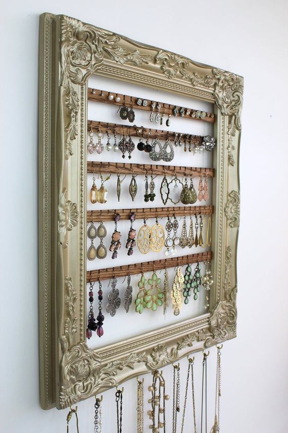 an ornate frame holds several pairs of earrings and earring hooks on a white wall