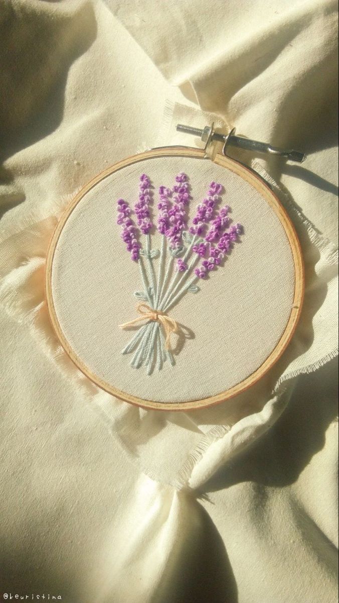 a close up of a cross stitch pattern with lavender flowers in the center on a white cloth