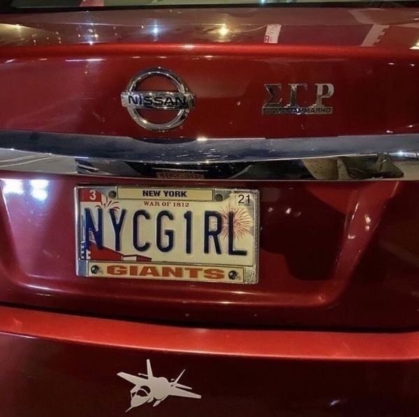 the front end of a red car with a new york girl license plate on it