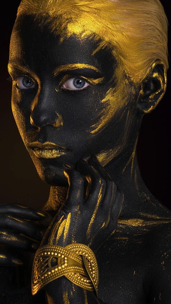 a woman with black and gold paint on her face is posing for the camera in front of a dark background