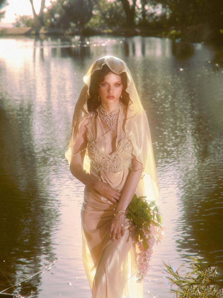 a woman in a wedding dress standing on the edge of a body of water wearing a veil