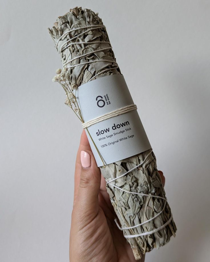 a person holding up a bundle of white sage with the words slow down written on it