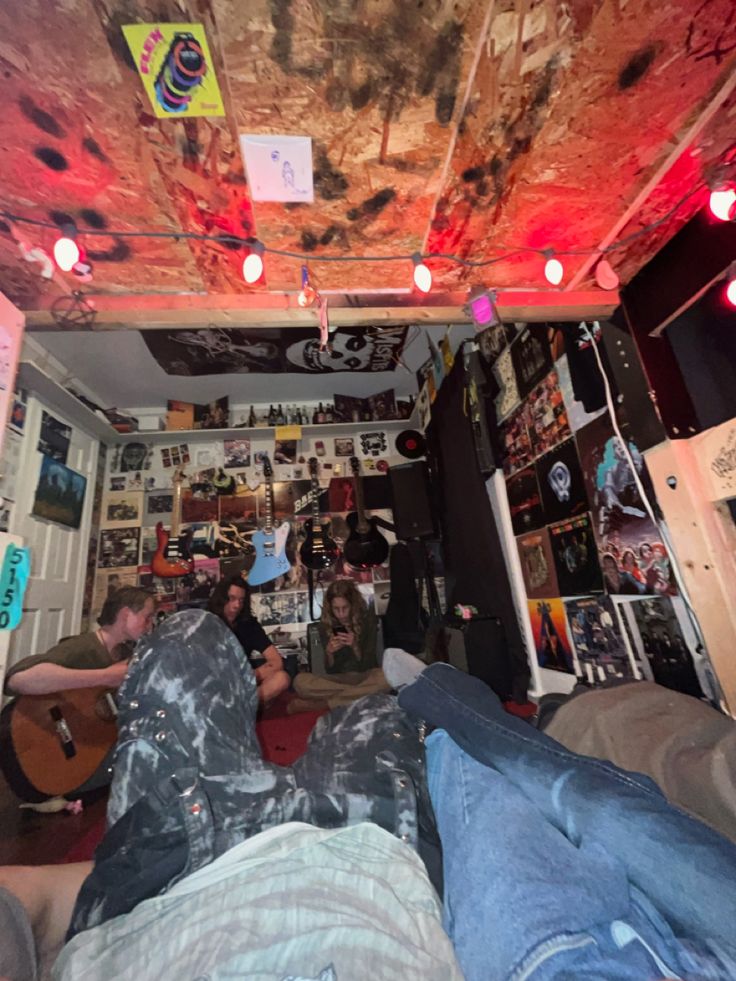 some people are laying down in a room with guitars and posters on the wall behind them