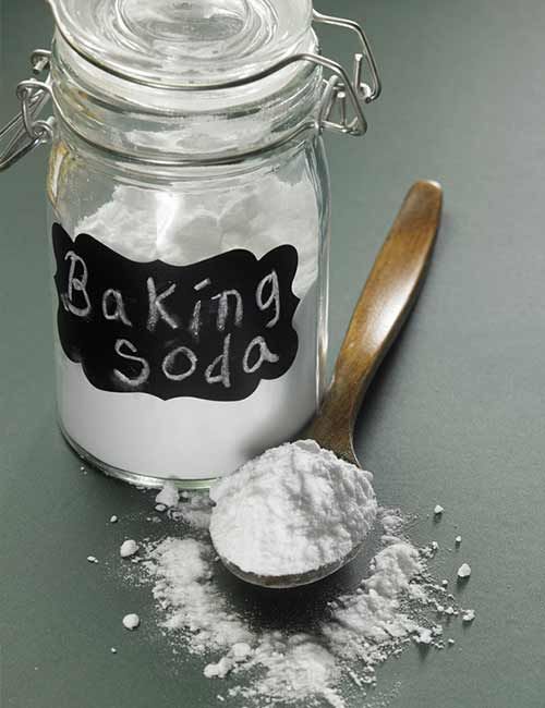 baking soda in a glass jar next to a wooden spoon